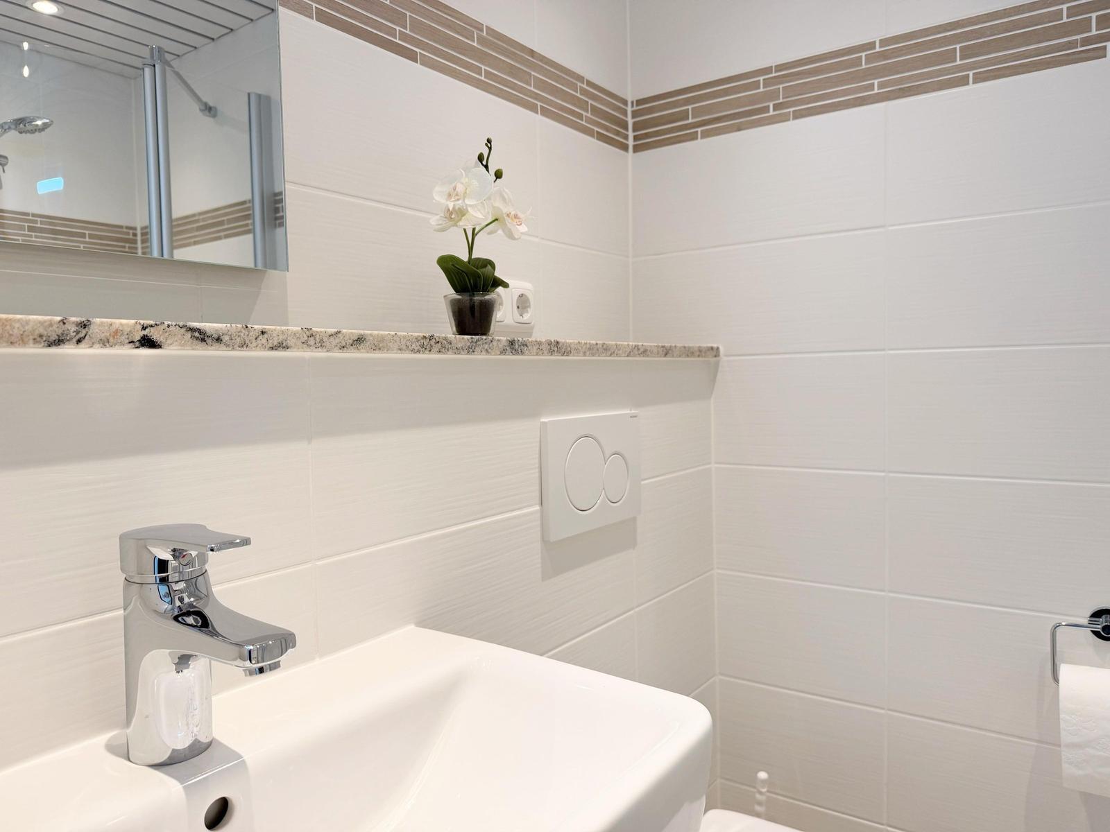 Badezimmer mit Waschbecken, Spiegel und Orchidee auf Marmorarbeitsplatte.