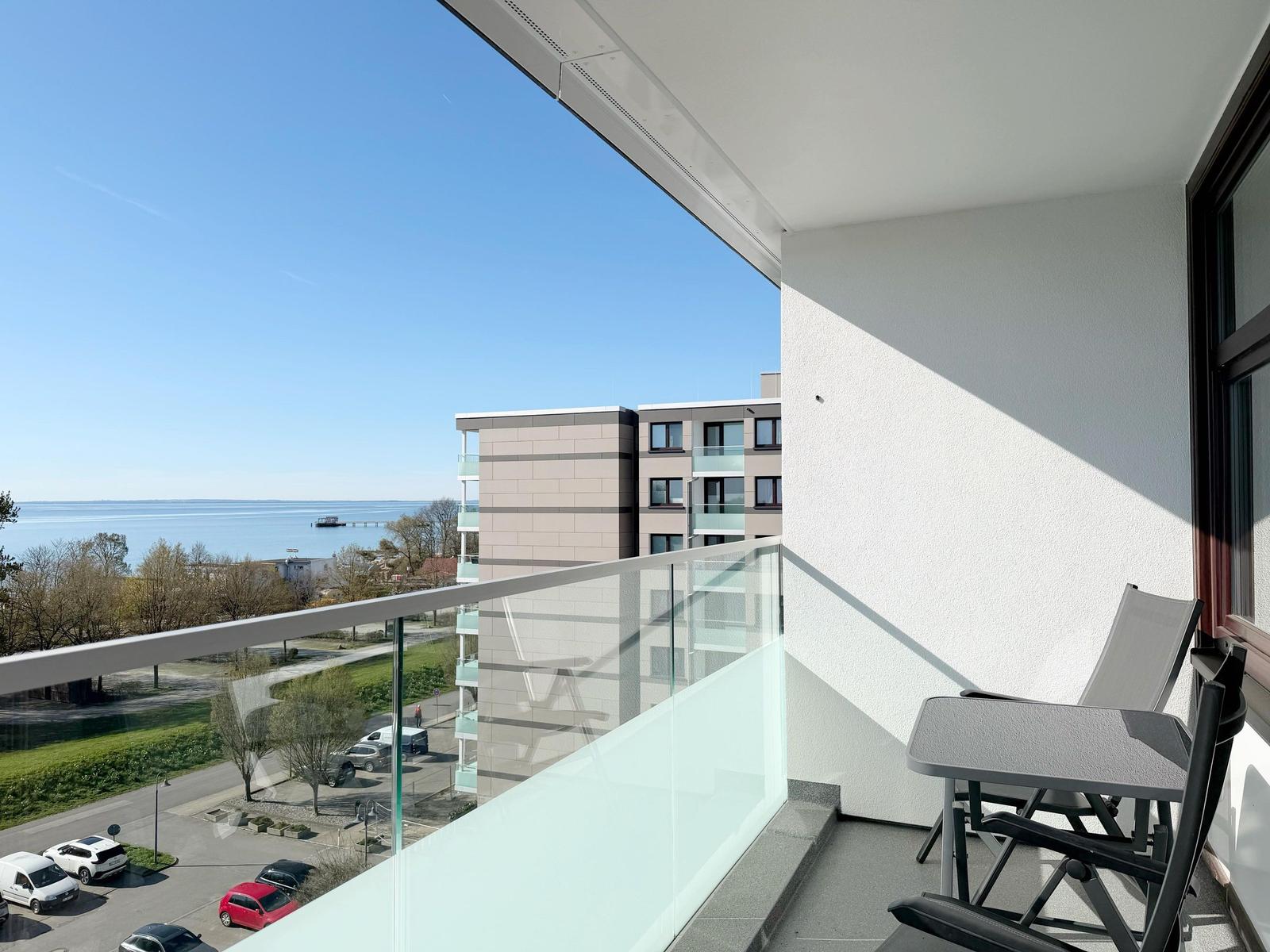 Balkon mit Tisch und Stühlen, Blick auf See und Gebäude.