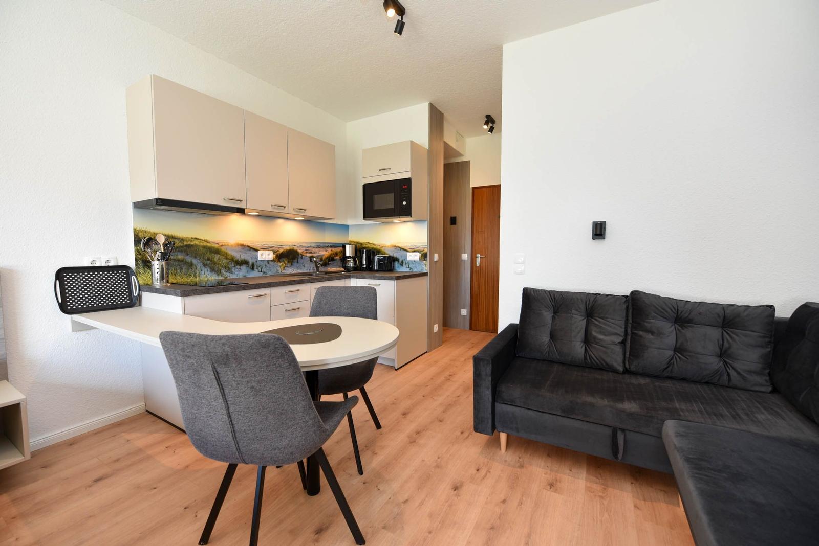 Wohnung mit Küche, Esstisch und Sofa. Holzfußboden und Wandbilder.