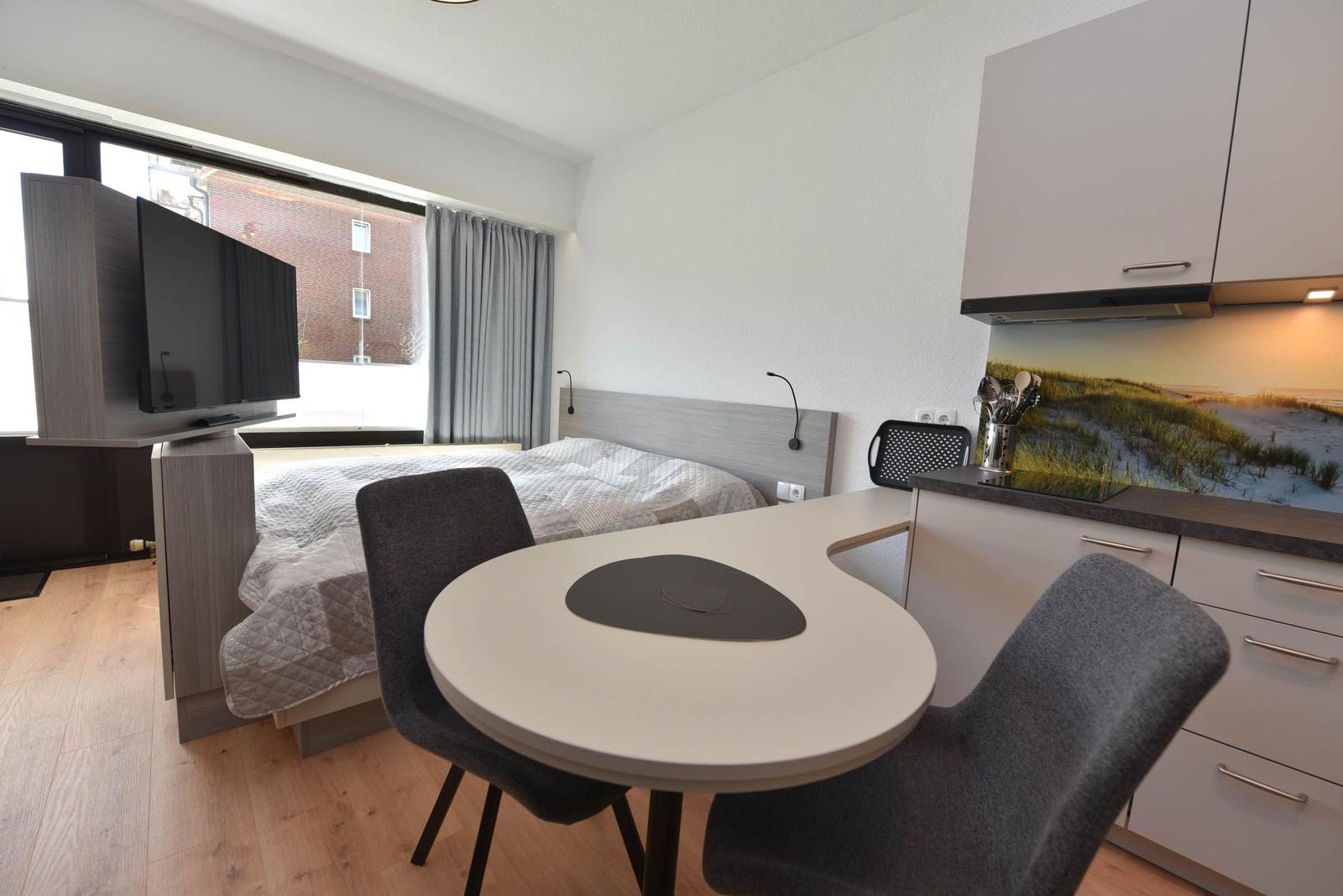 Schlafzimmer mit Bett, TV und Küchenbereich mit Tisch und Stühlen.