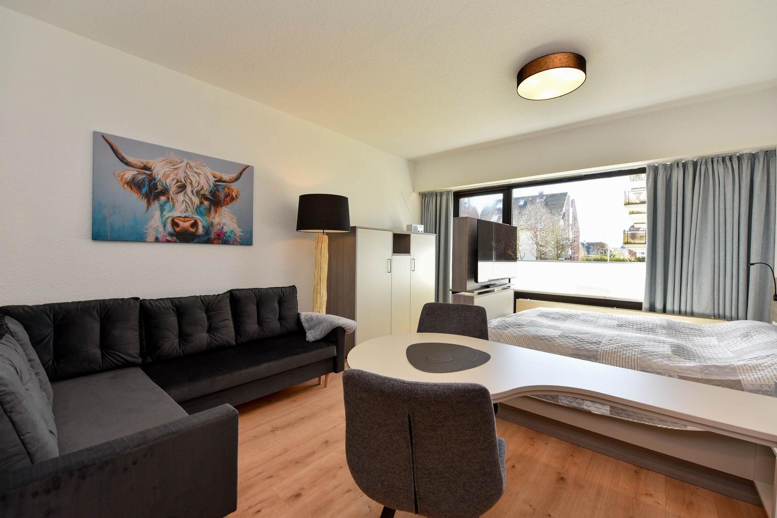 Ein Raum mit Sofa, Bett und Tisch. An der Wand hängt ein Bild eines Hochlandrindes.
