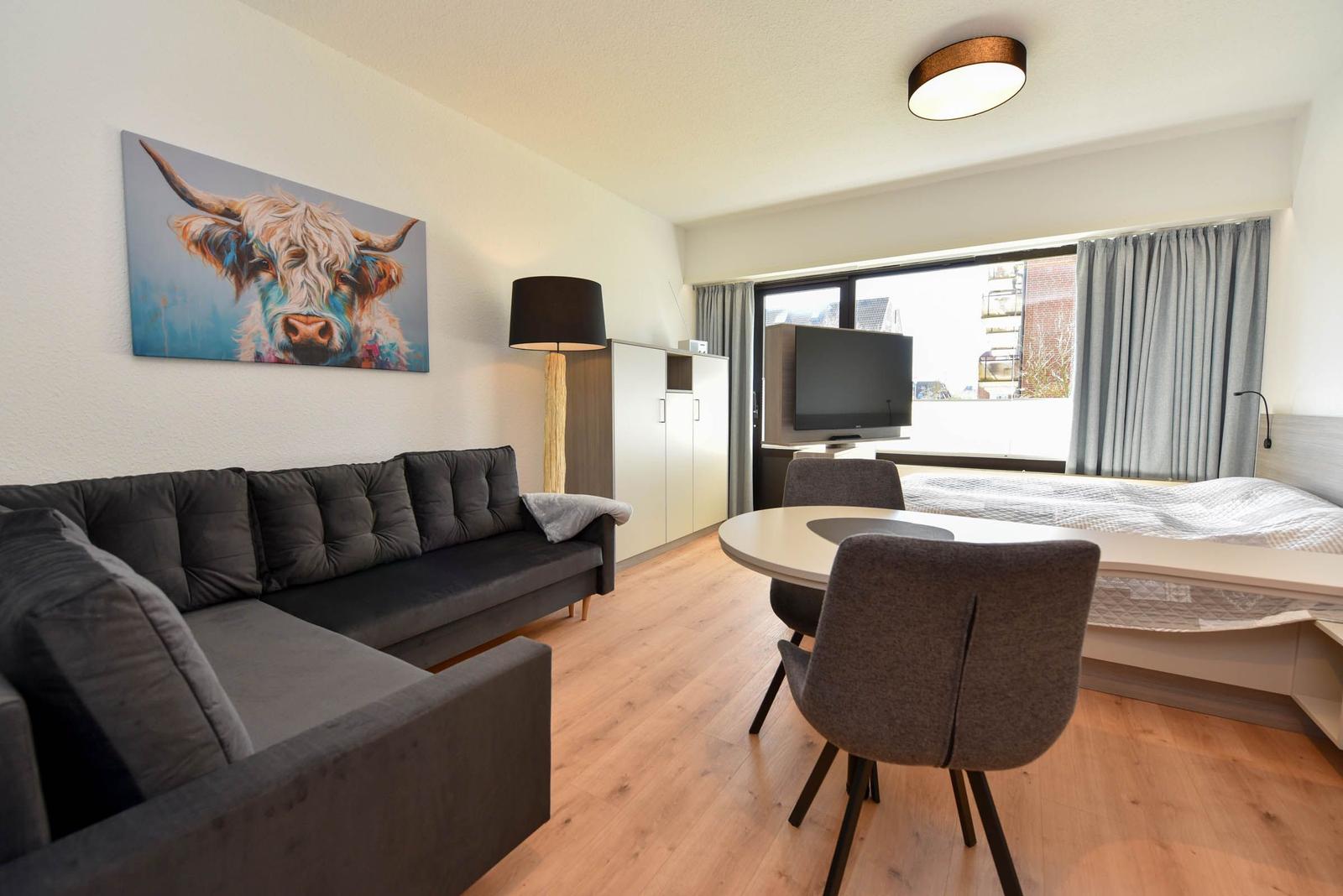 Wohnung mit Sofa, Esstisch, Bett und Wandbild eines Highland-Rindes.