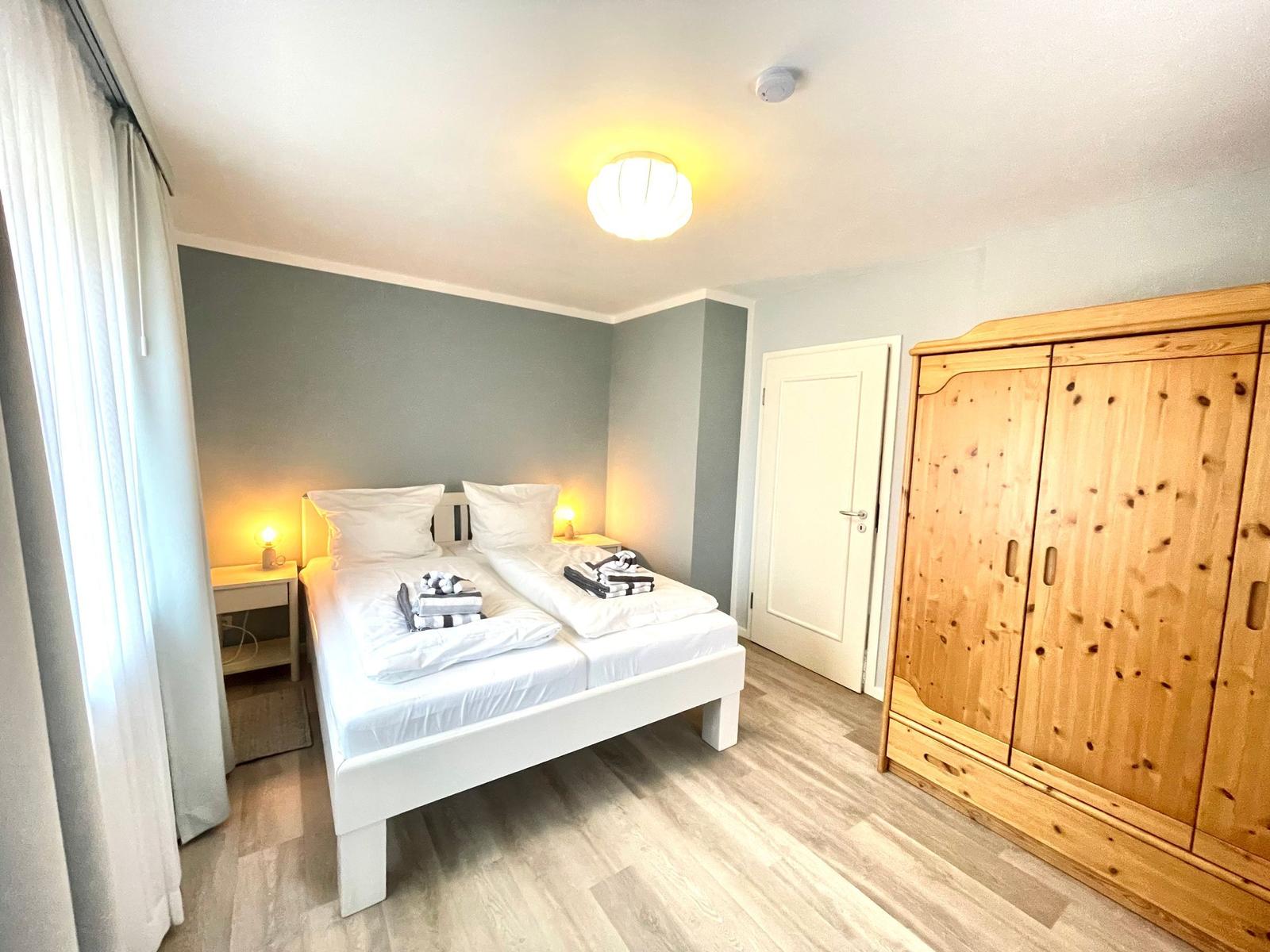 Schlafzimmer mit Doppelbett, Holzschrank und Nachttischen mit Lampen.