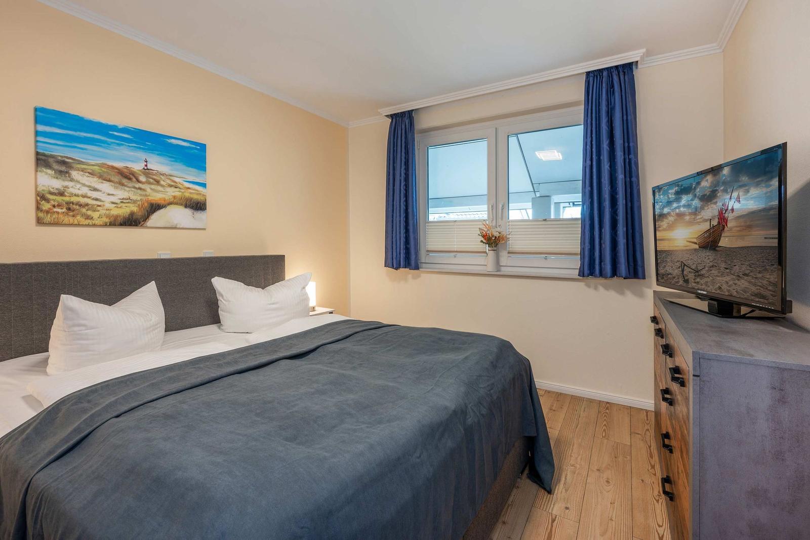 Schlafzimmer mit Doppelbett, Fenster, TV und Wandbild.