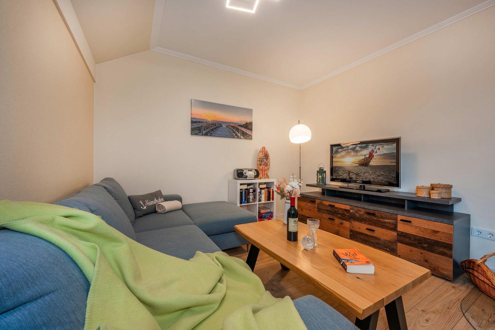 Wohnzimmer mit Sofa, Couchtisch und Fernseher. Wandbild und Bücherregal sichtbar.