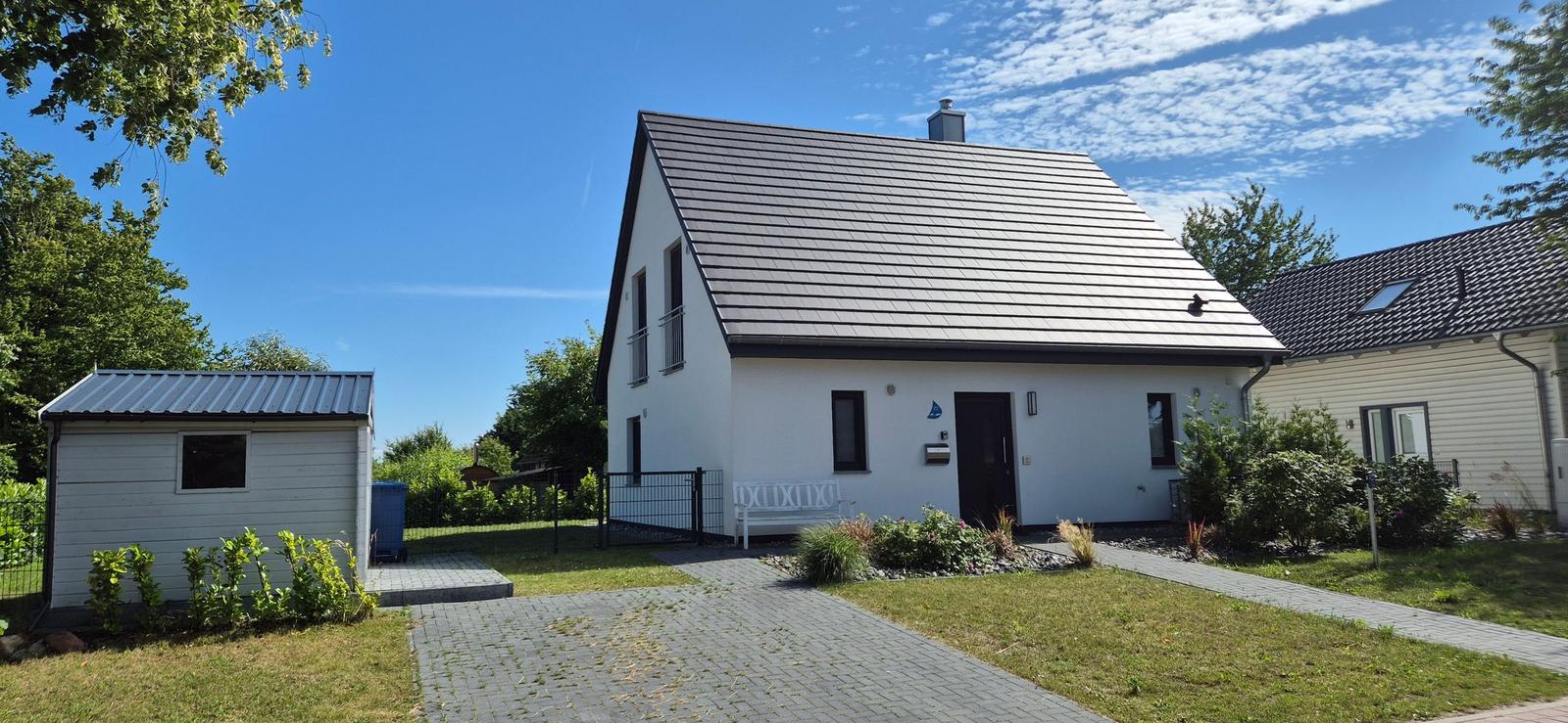 Moderne weiße Villa mit dunklem Dach, Garten und kleinem Nebengebäude.