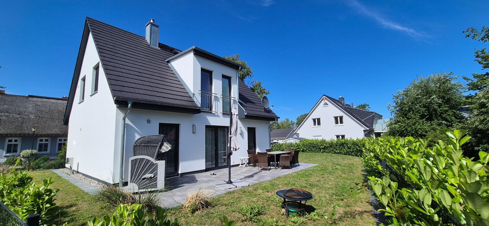 Modernes Haus mit Terrasse und Garten. Außentisch, Sitzgruppe und Grill sind vorhanden.