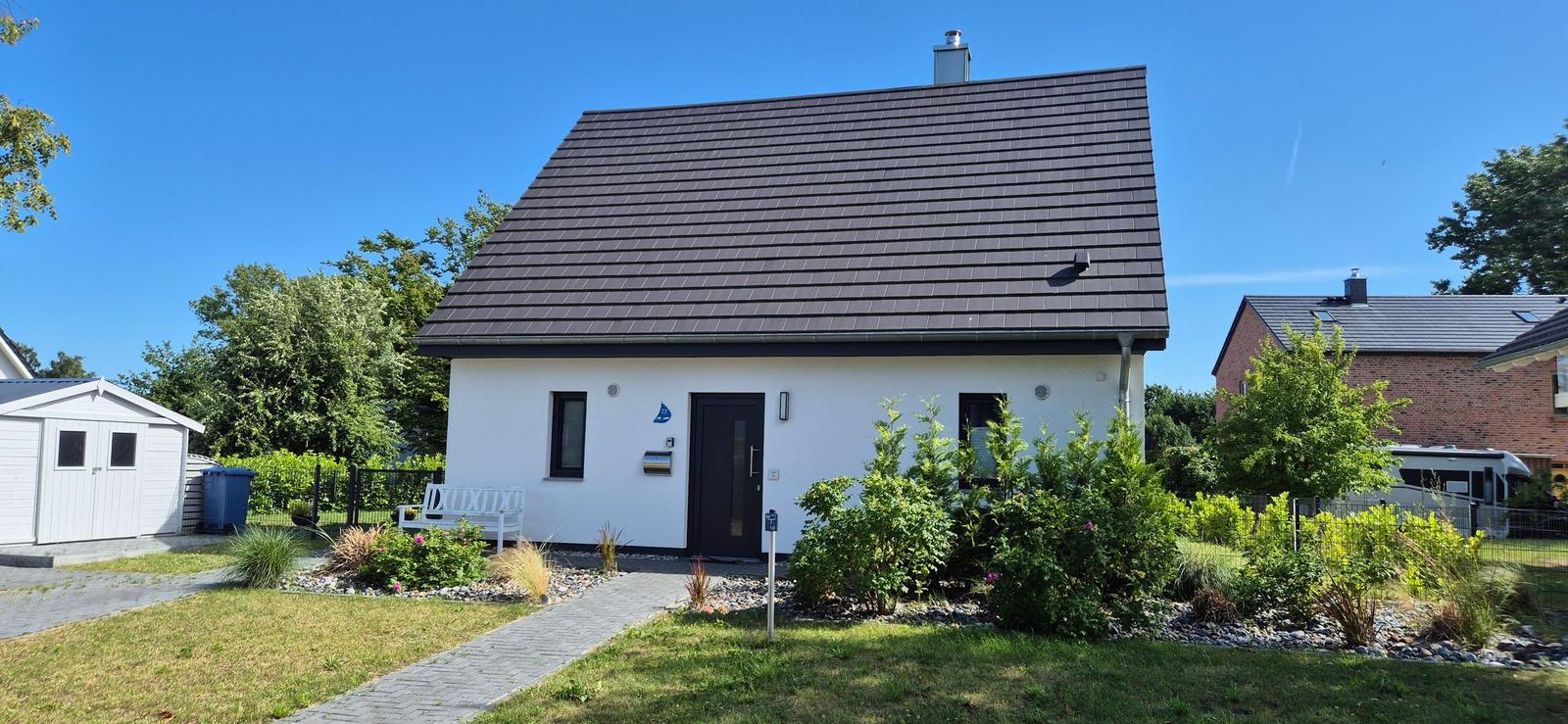 Ein weißes Haus mit dunklem Dach, Vorgarten und weiße Bank.