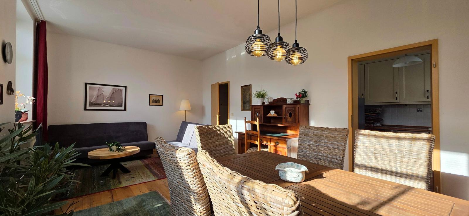 Dining area with table and chairs, living area with sofa and coffee table, kitchen area in background.