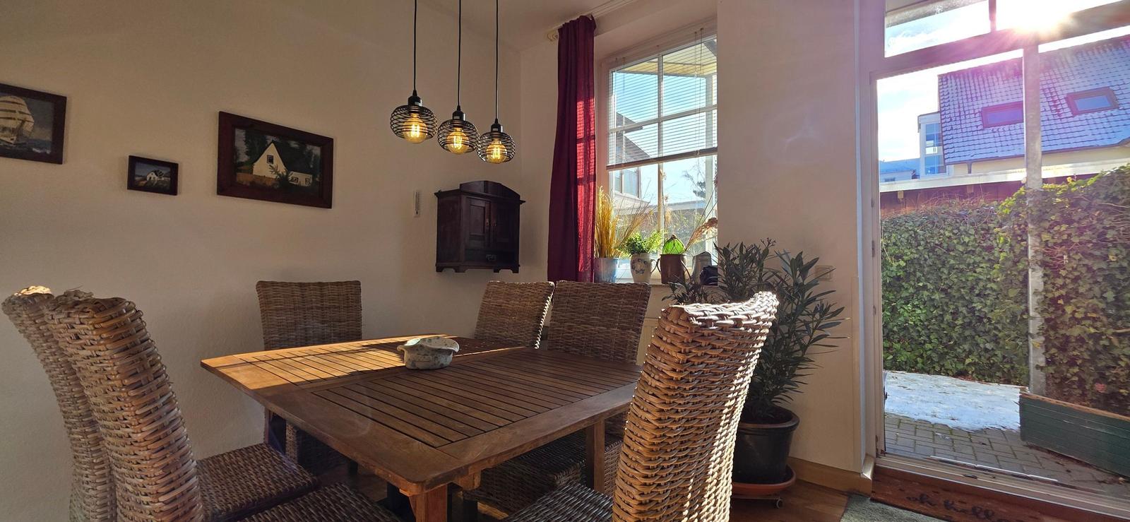 Dining room with wooden table, rattan chairs, and garden view through window.