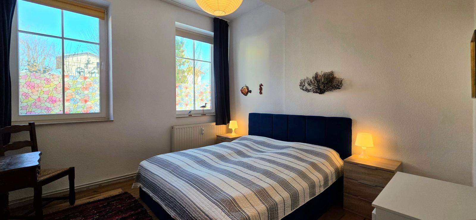 Bedroom with bed, two windows, and nightstands with lamps.