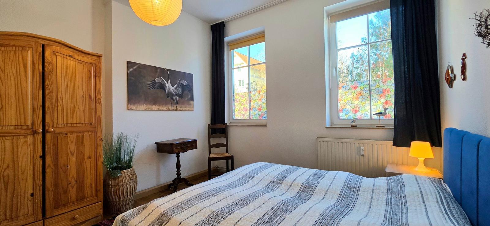 Bedroom with bed, wardrobe, and windows with colorful glass panels.