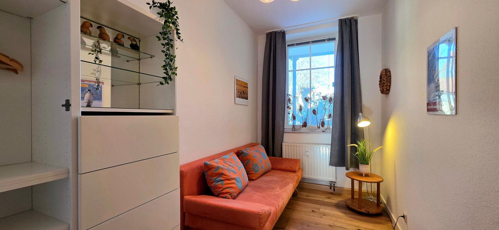 A room with an orange sofa, wooden floor, and window with curtains.