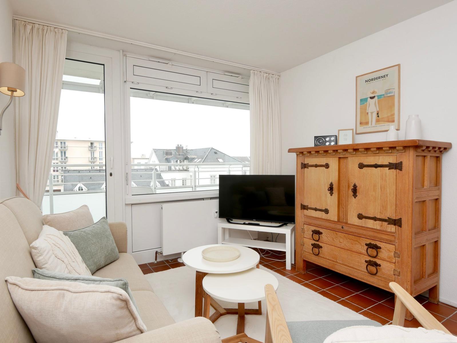 Wohnzimmer mit Sofa, TV und Holzschrank. Balkon mit Blick auf Gebäude.