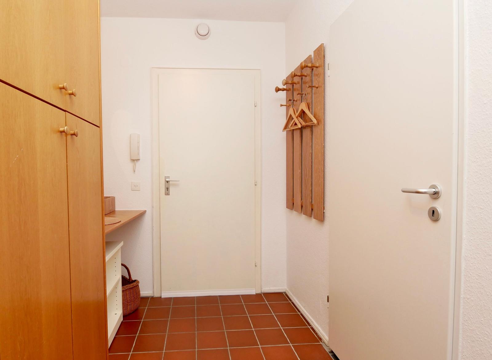 Eingangsbereich mit Holzgarderobe, Tür und Terrakottaboden.