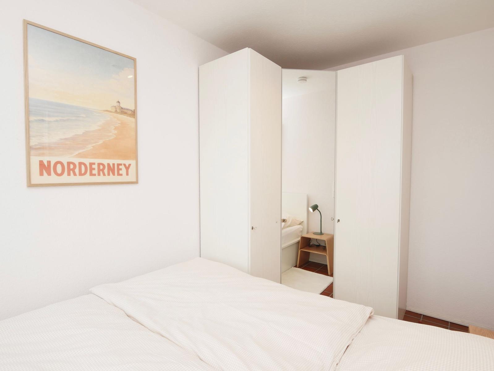 Schlafzimmer mit weißem Bett, Kleiderschrank und Wandbild von Norderney.