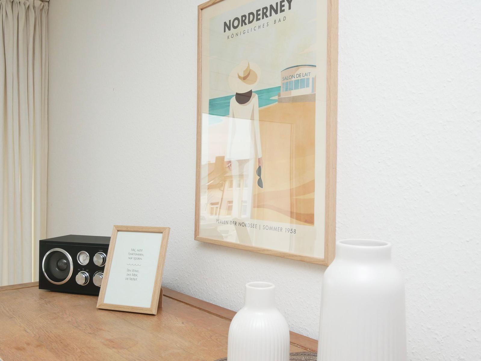 Wandbild mit Nordsee-Thema, Tisch mit Lautsprecher und Vasen.