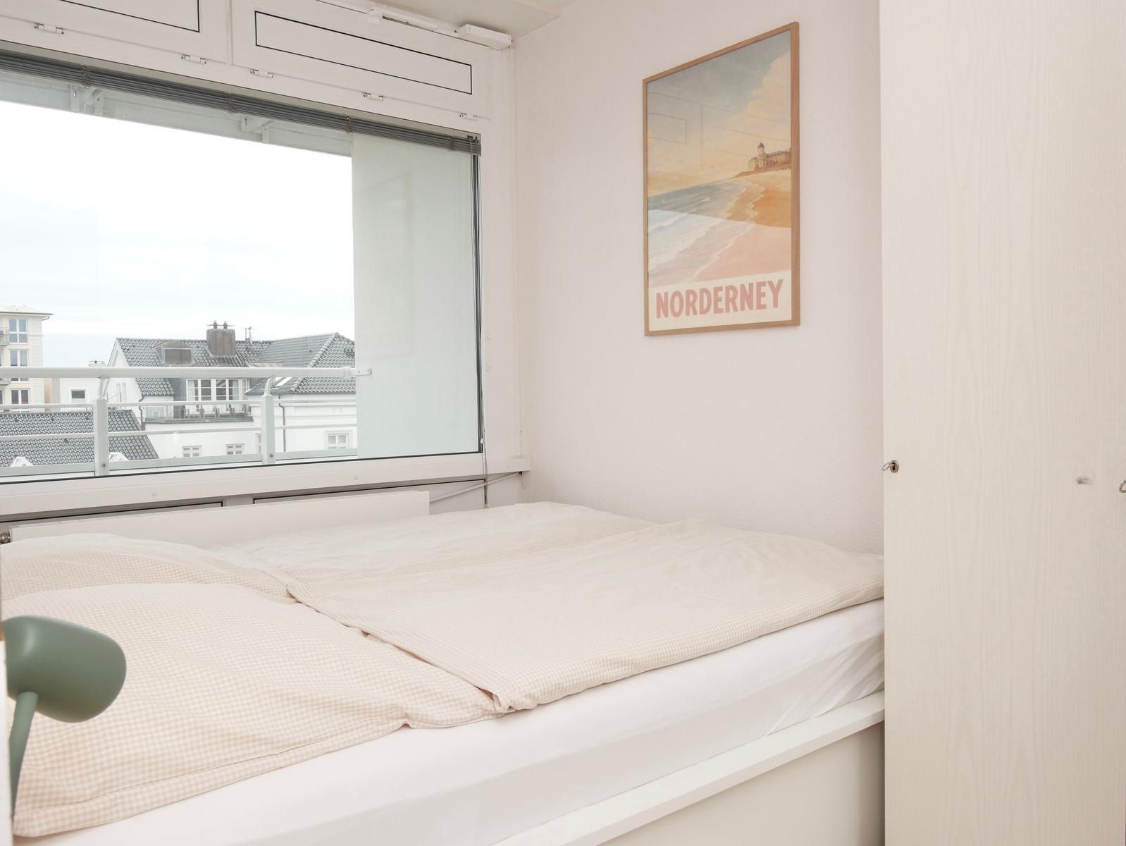 Schlafzimmer mit Bett, Fenster und Wandbild von Norderney.