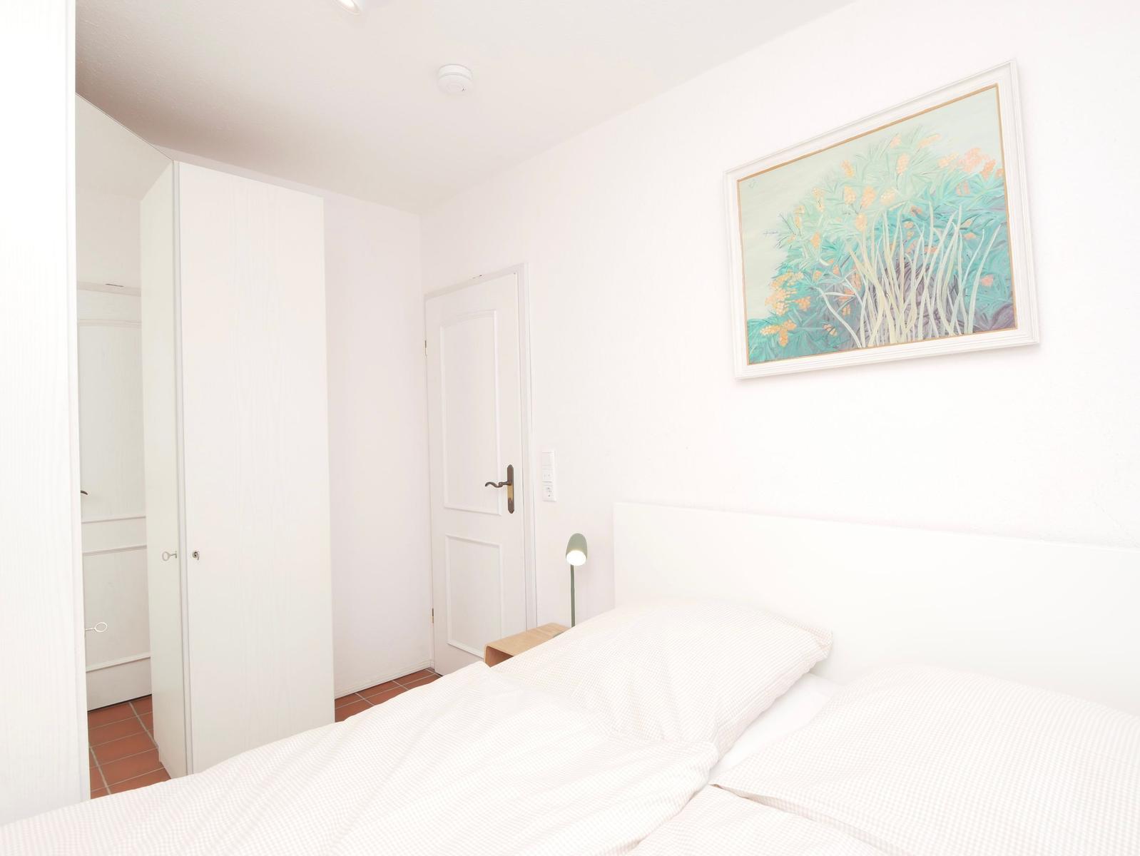 Schlafzimmer mit Bett, Wandbild und Kleiderschrank. Tür und Nachttisch sind sichtbar.