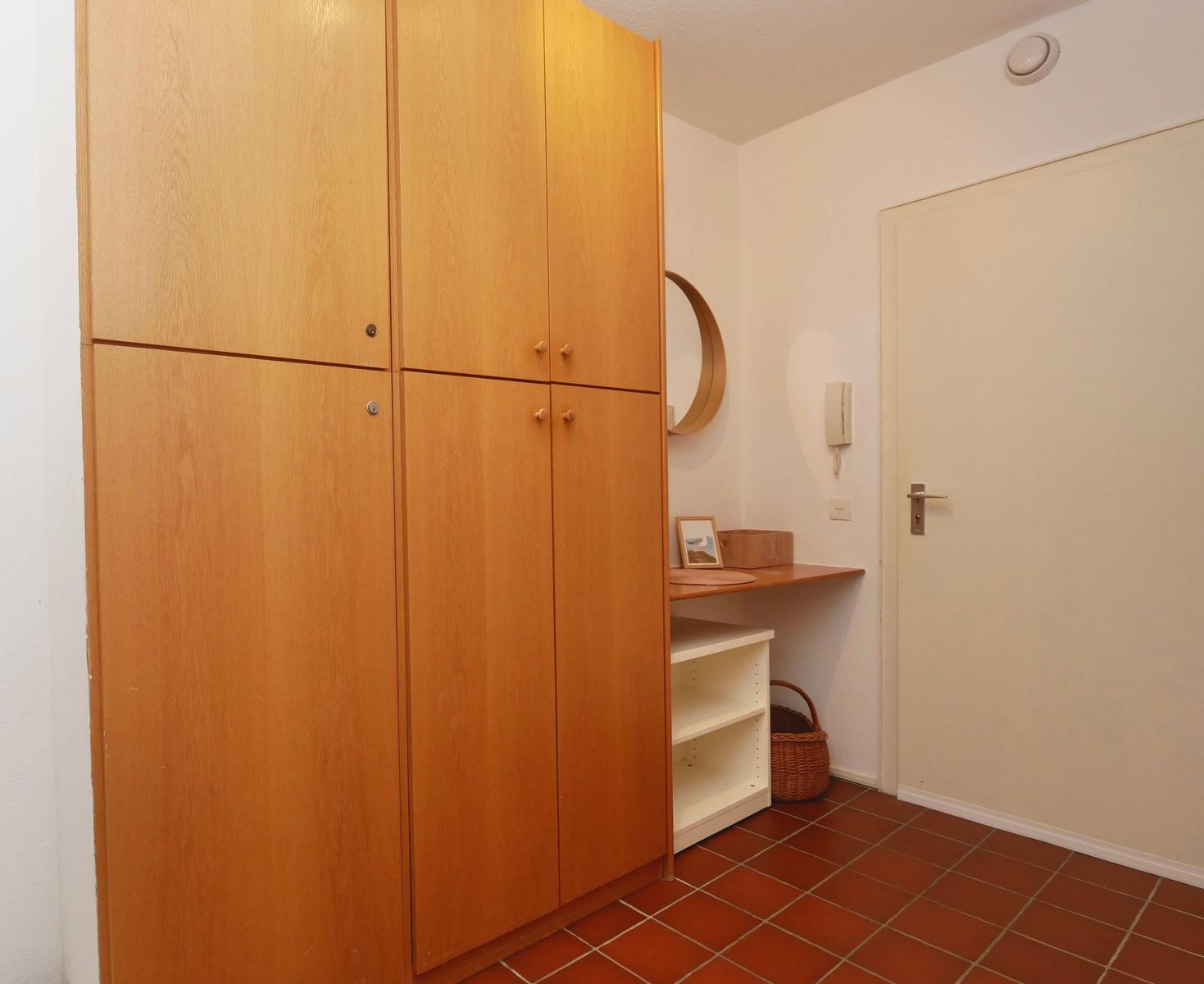 Eingangsbereich mit Holzschrank, kleinem Tisch und Tür.