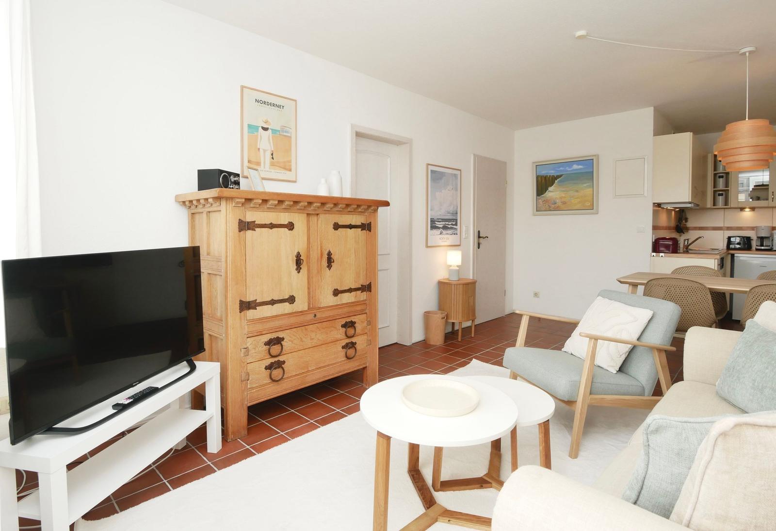 Wohnzimmer mit TV, Holzschrank, Sitzgruppe und Küchenbereich im Hintergrund.