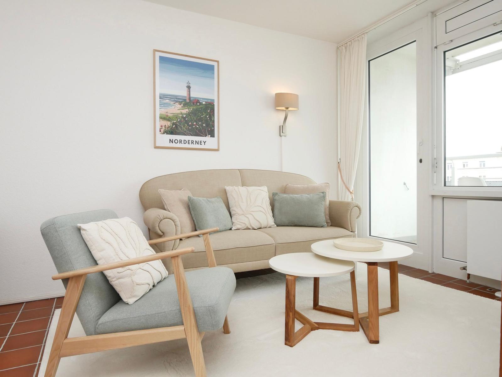 Wohnzimmer mit Sofa, Sessel, Tischen und Wandbild von Norderney.