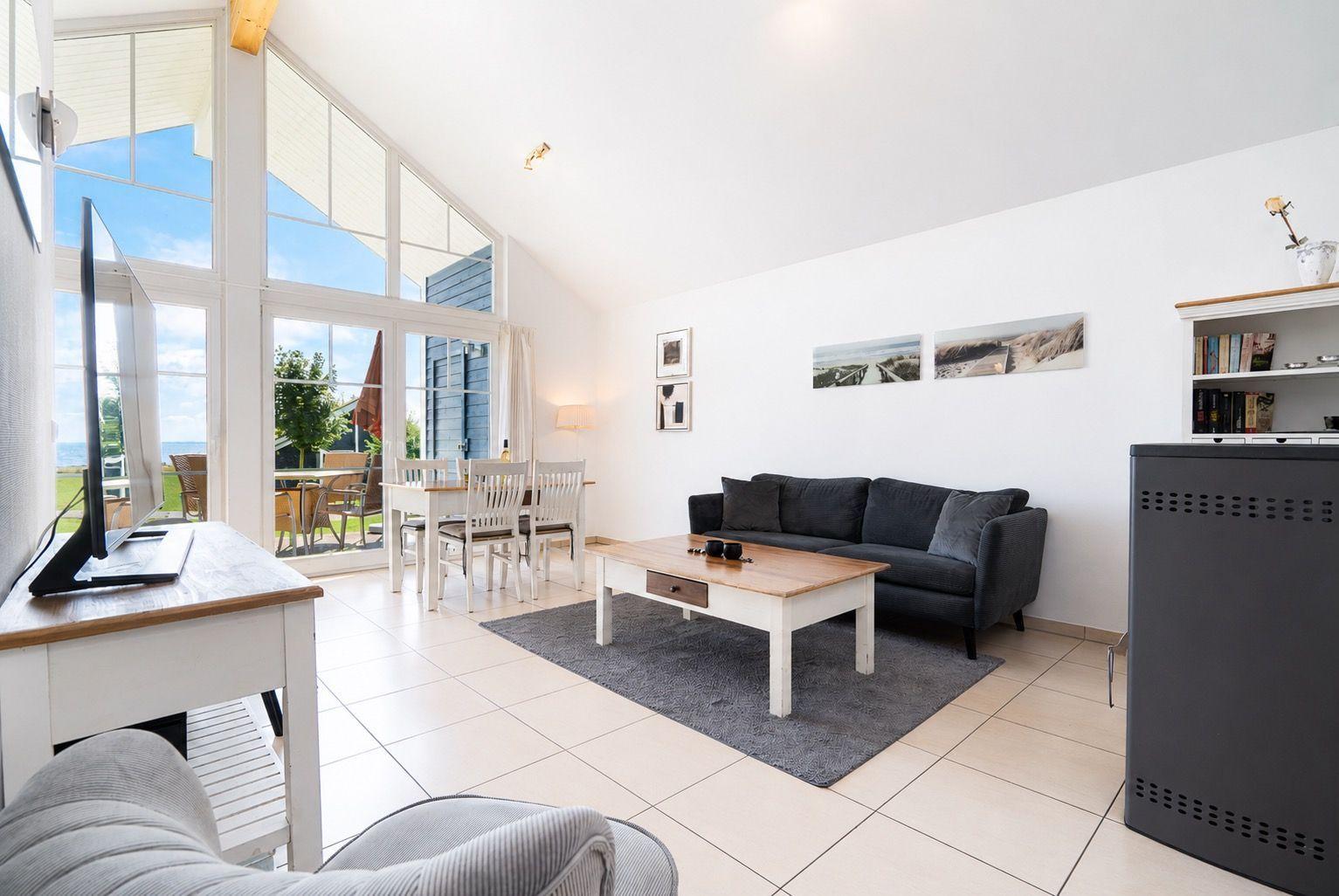 Living room with sofa, coffee table, and TV. Large windows with sea view.