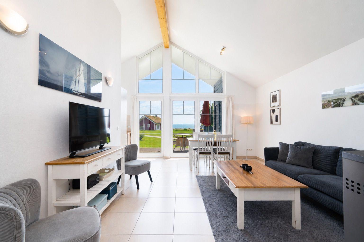 Living room with sofa, dining table, and large window overlooking the sea.