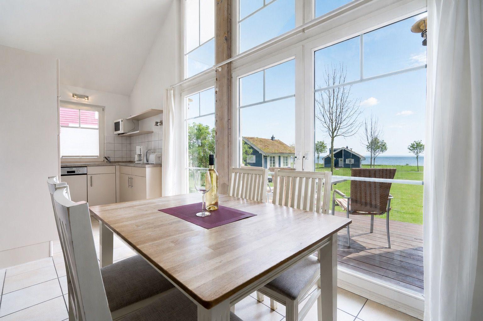 Dining area with table and chairs. Large windows offer view of terrace and beach.