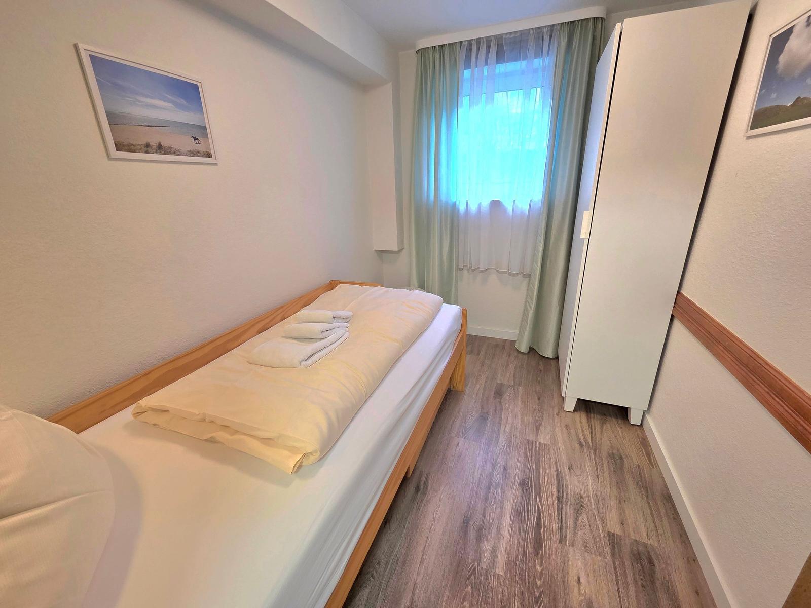 Schlafzimmer mit Bett, Kleiderkabinett und Fenster mit Vorhängen.