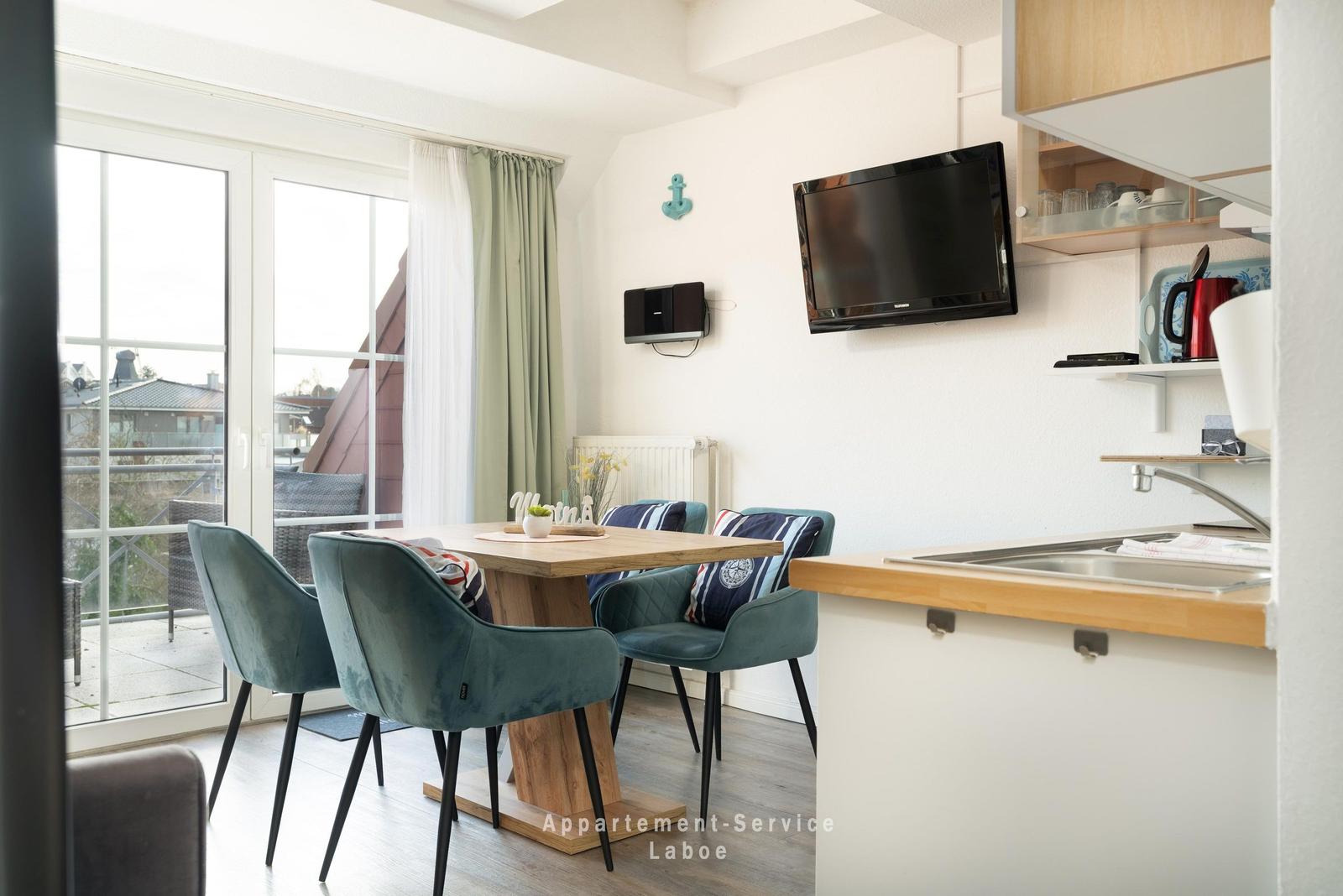 Essbereich mit Tisch und Stühlen, TV und Küchenzeile mit Fenster zur Terrasse.
