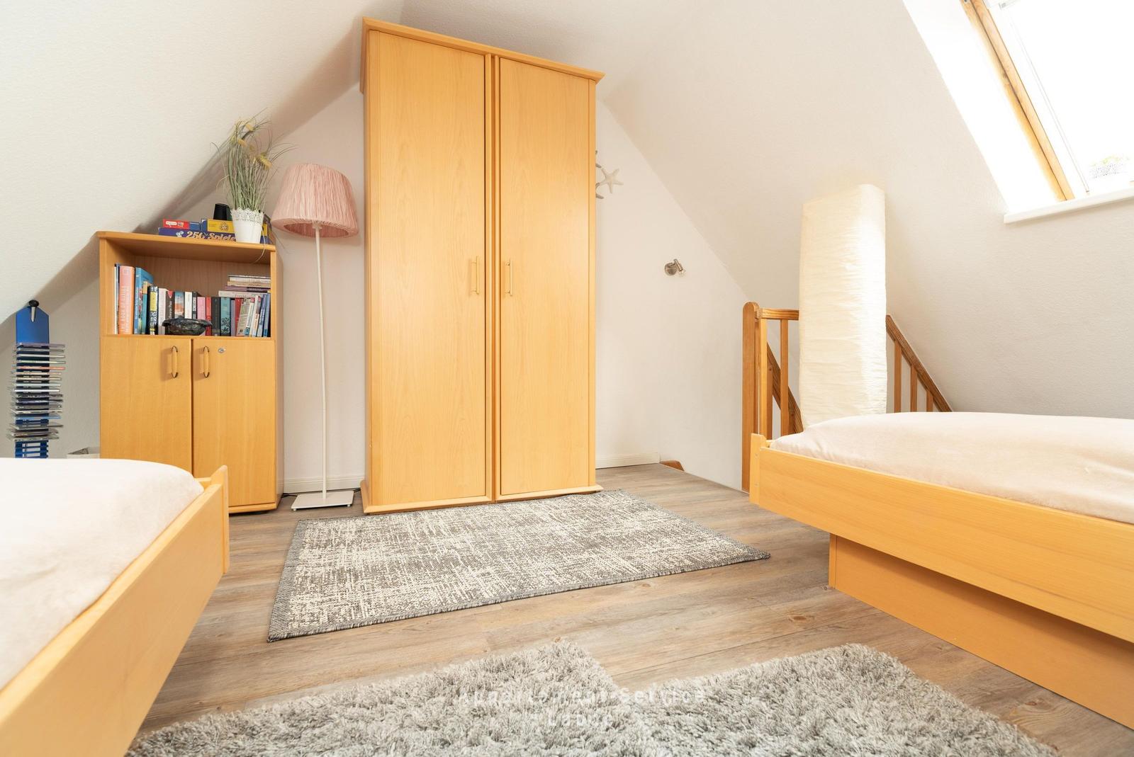 Zimmer mit zwei Betten, Kleiderschrank und Bücherregal unter Dachschrägen.