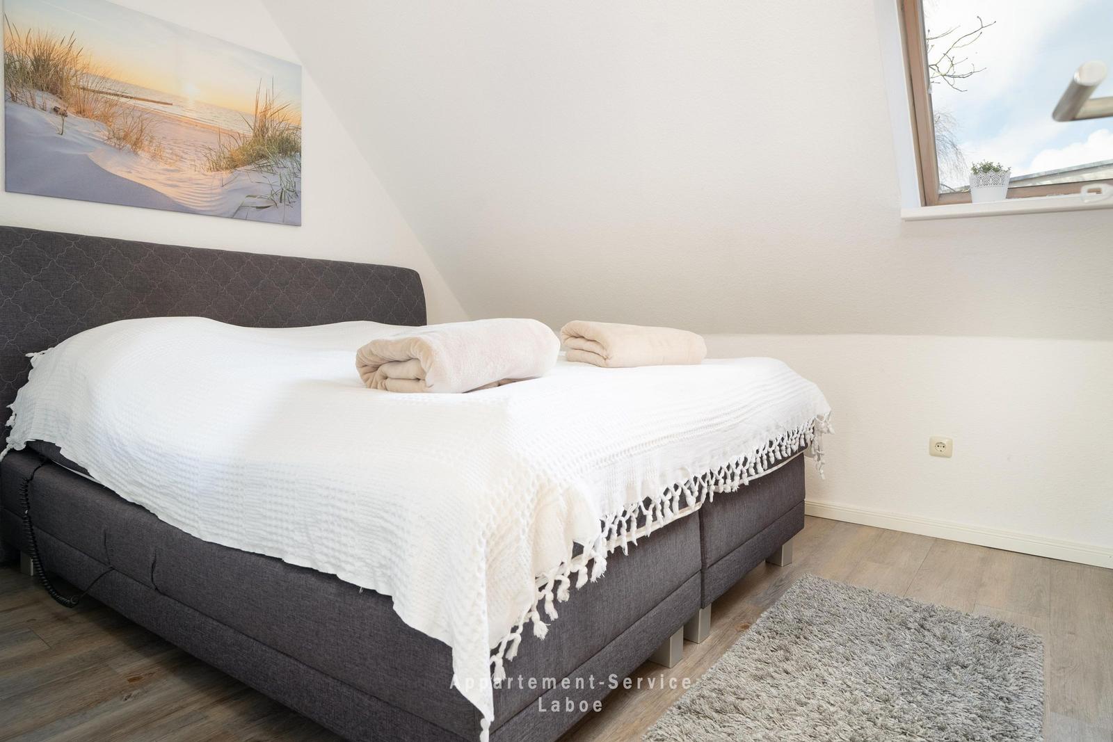 Ein Schlafzimmer mit Bett, Fenster und Wandbild. Holzfußboden und Teppich.