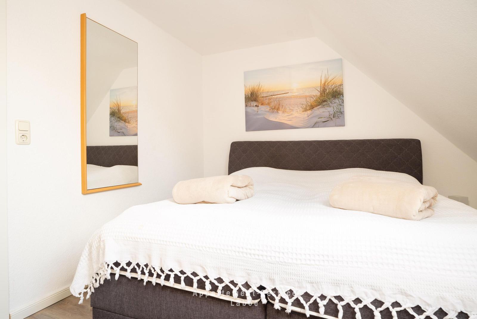 Schlafzimmer mit Bett, Wandspiegel und Strandbild an der Wand.