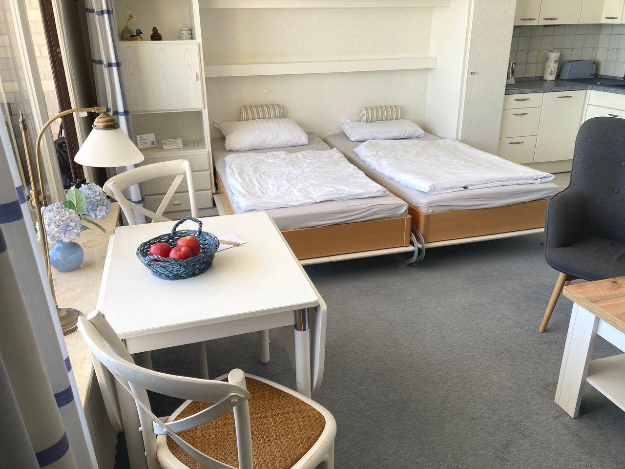 Two beds, table with chairs, kitchen area, and window with curtains.