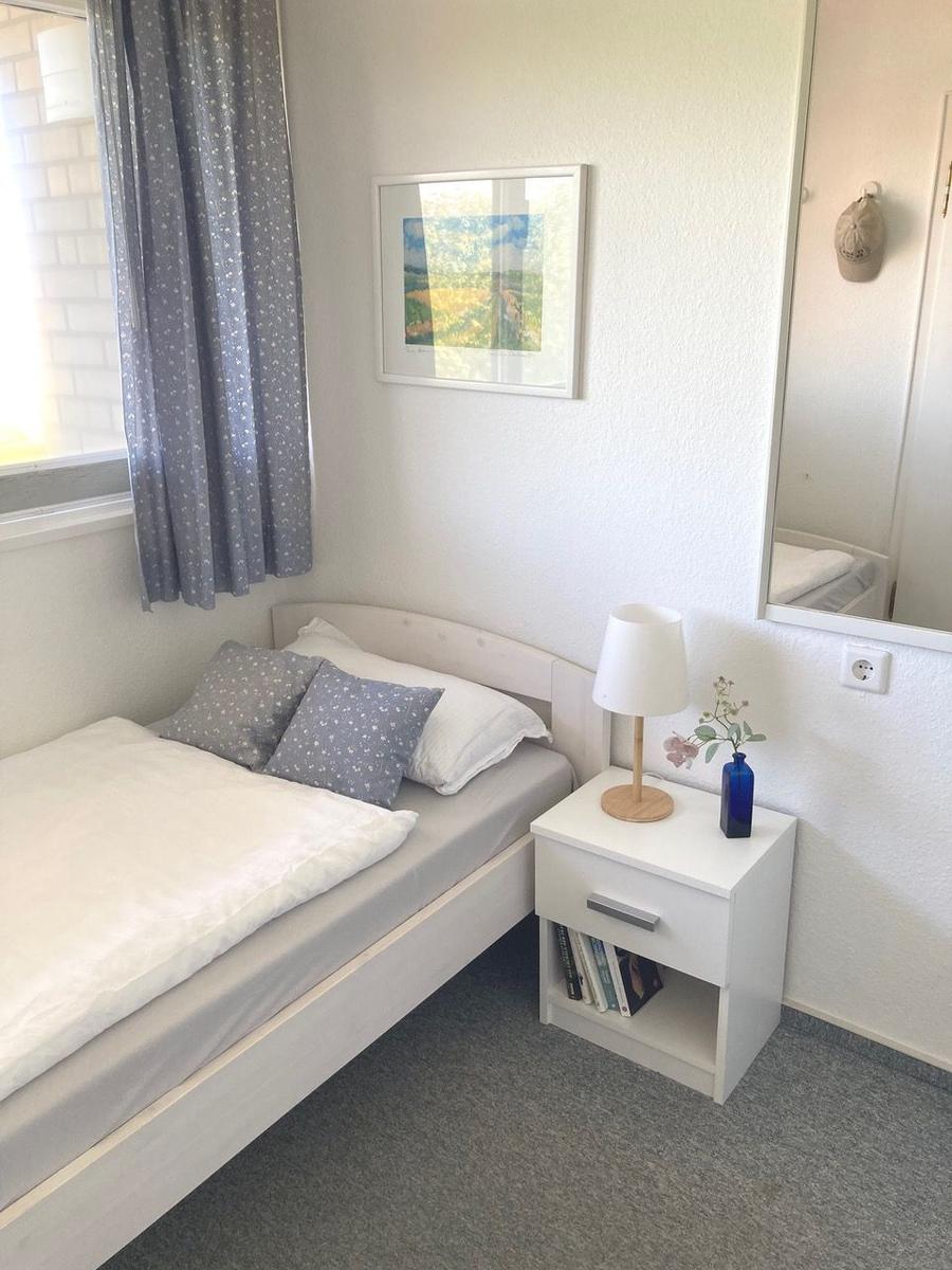 A bedroom with bed, nightstand, lamp, and picture on the wall.