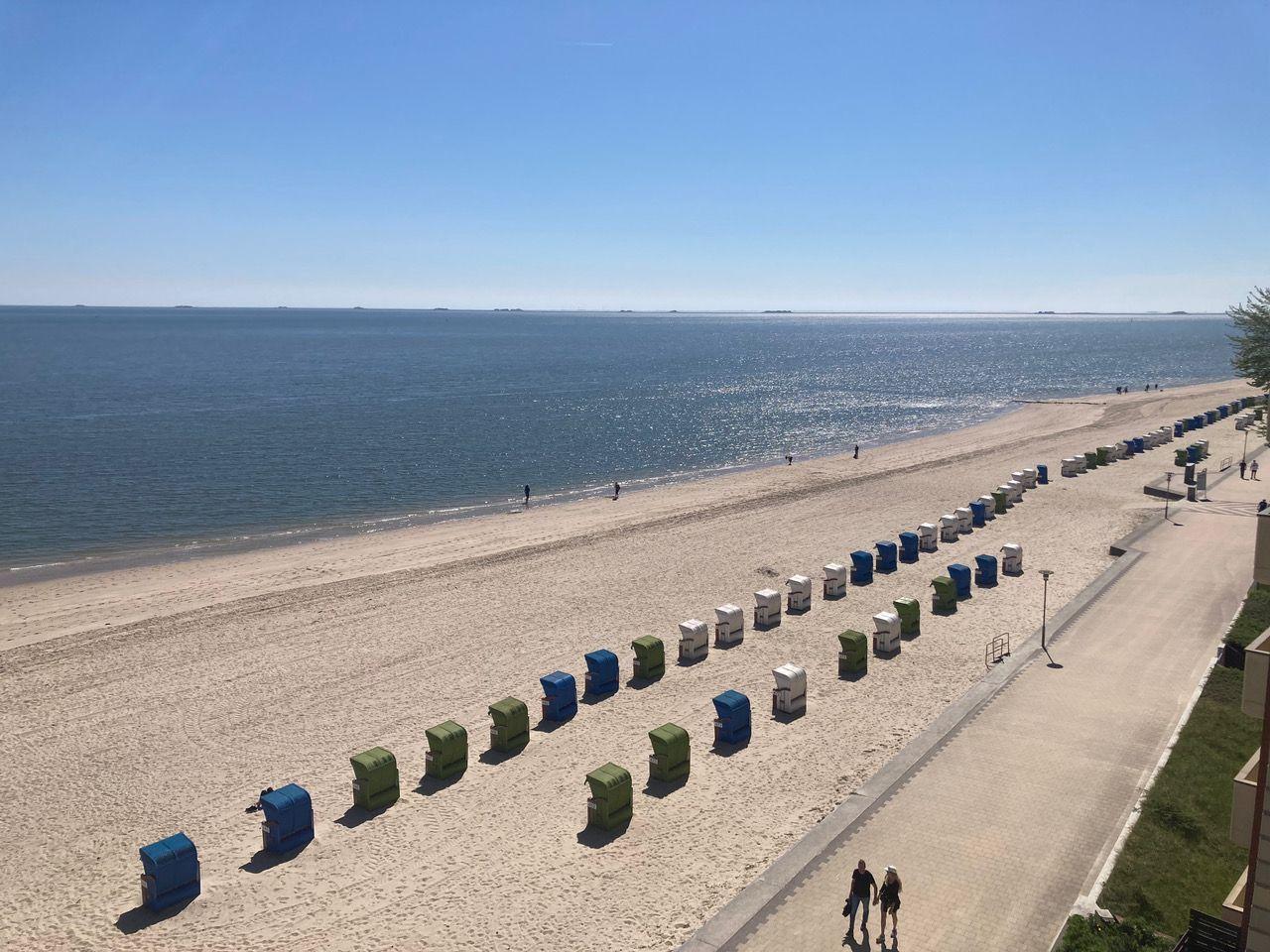 Beach with colorful beach chairs and promenade. View of the sea under blue sky.