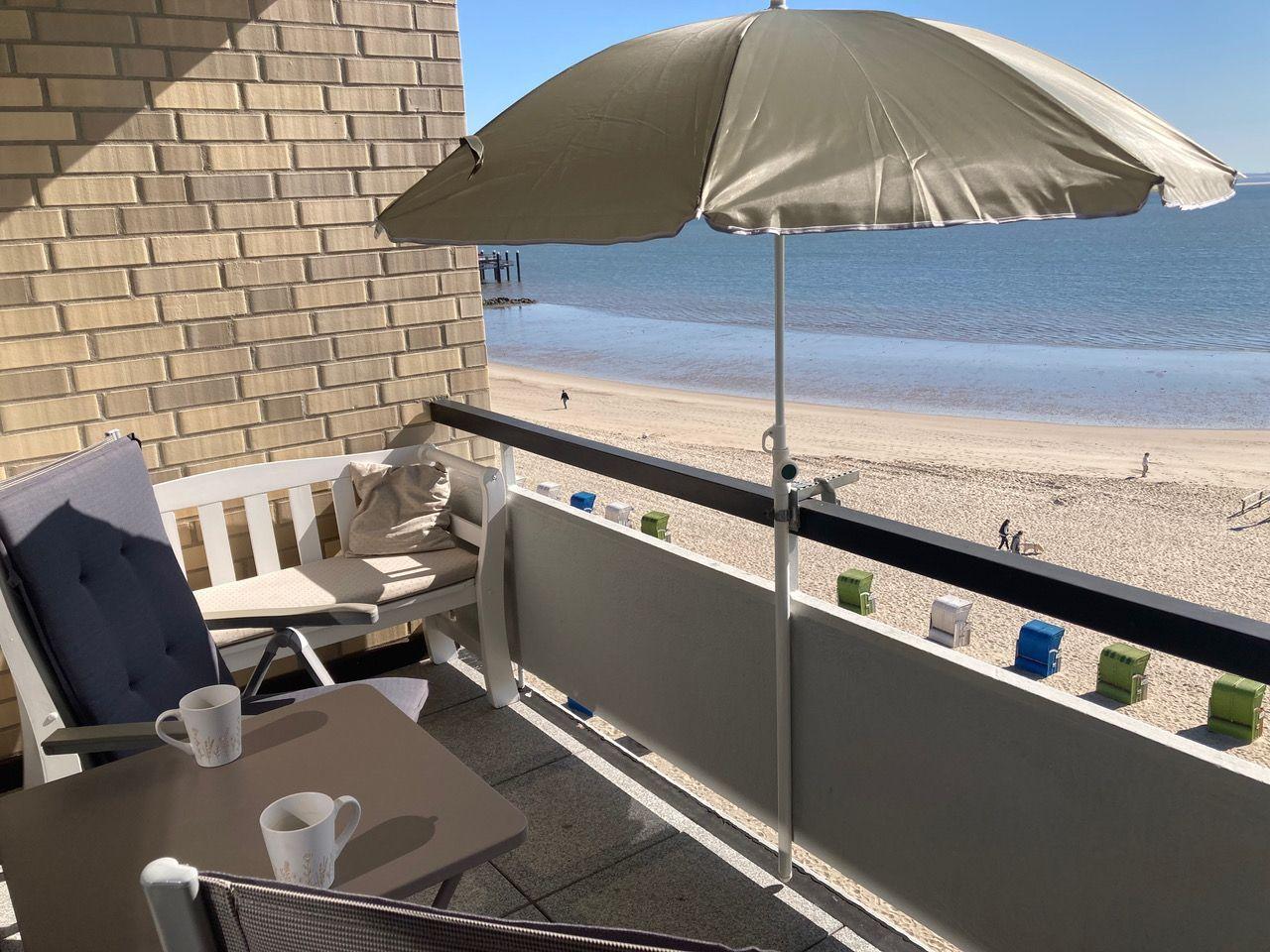 Balcony with umbrella, table, and chairs, view of beach and sea.