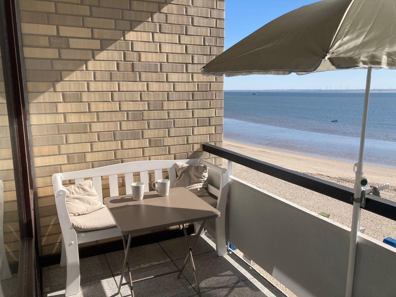 Terrace with table, chair, and umbrella. View of beach and sea.