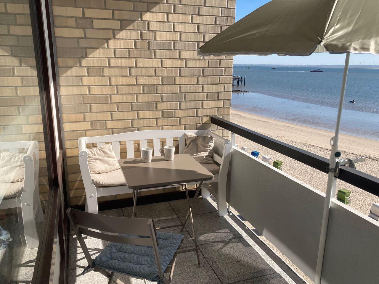 Terrace with table, chairs, and umbrella. View of beach and water.