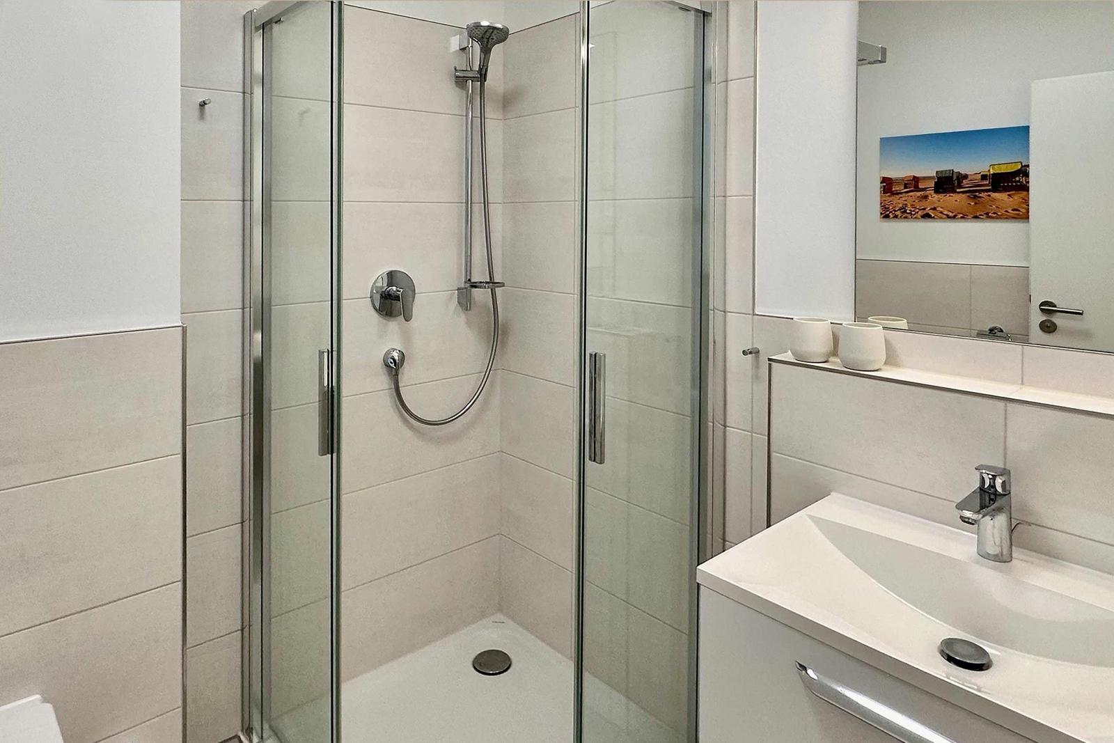 Dusche mit Glaswand, Waschbecken und Spiegel mit Wandbild.