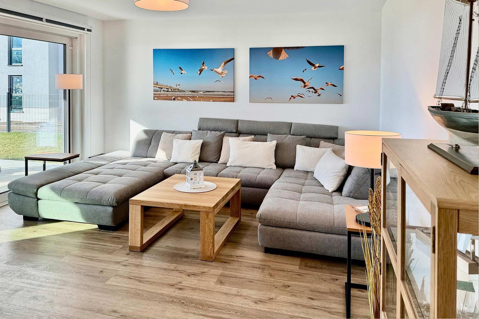 Wohnzimmer mit grauem Sofa, Holztisch und Wandbildern von Seemöwen.