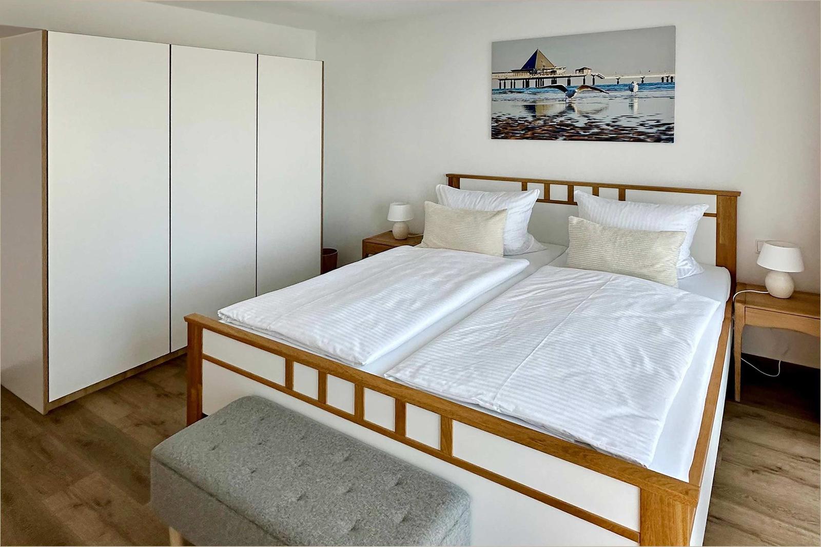 Doppelbett mit weißen Bettwäsche, Holzrahmen, zwei Nachttische und Kleiderschrank.