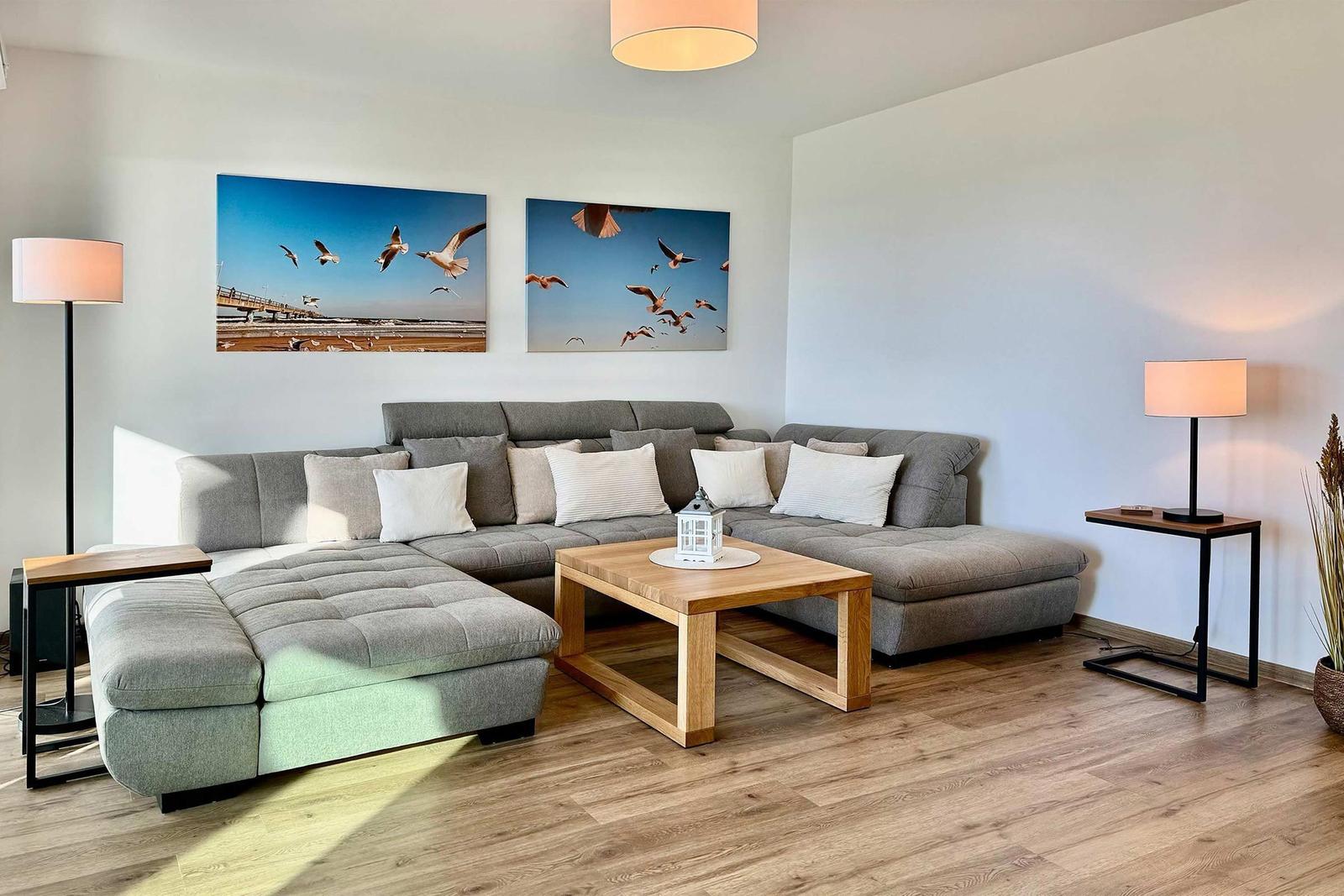 Wohnzimmer mit grauem Sofa, Holztisch und Wandbildern von Seeadlern.