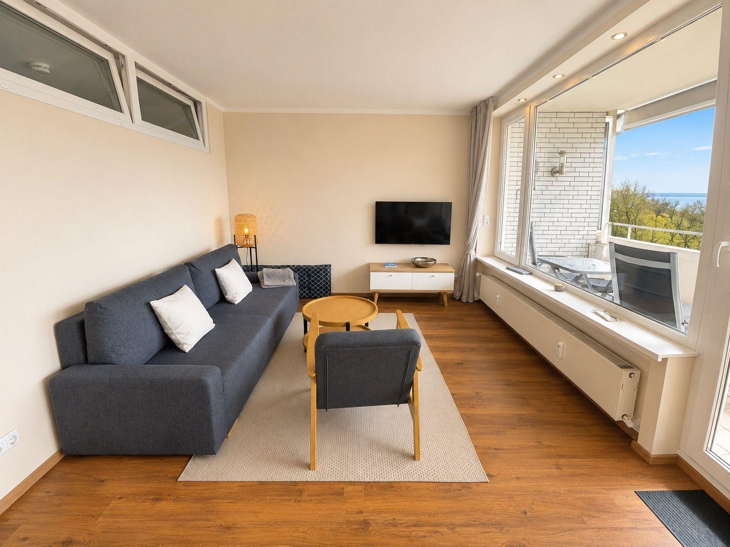 Living room with sofa, armchair, TV, and balcony with sea view.