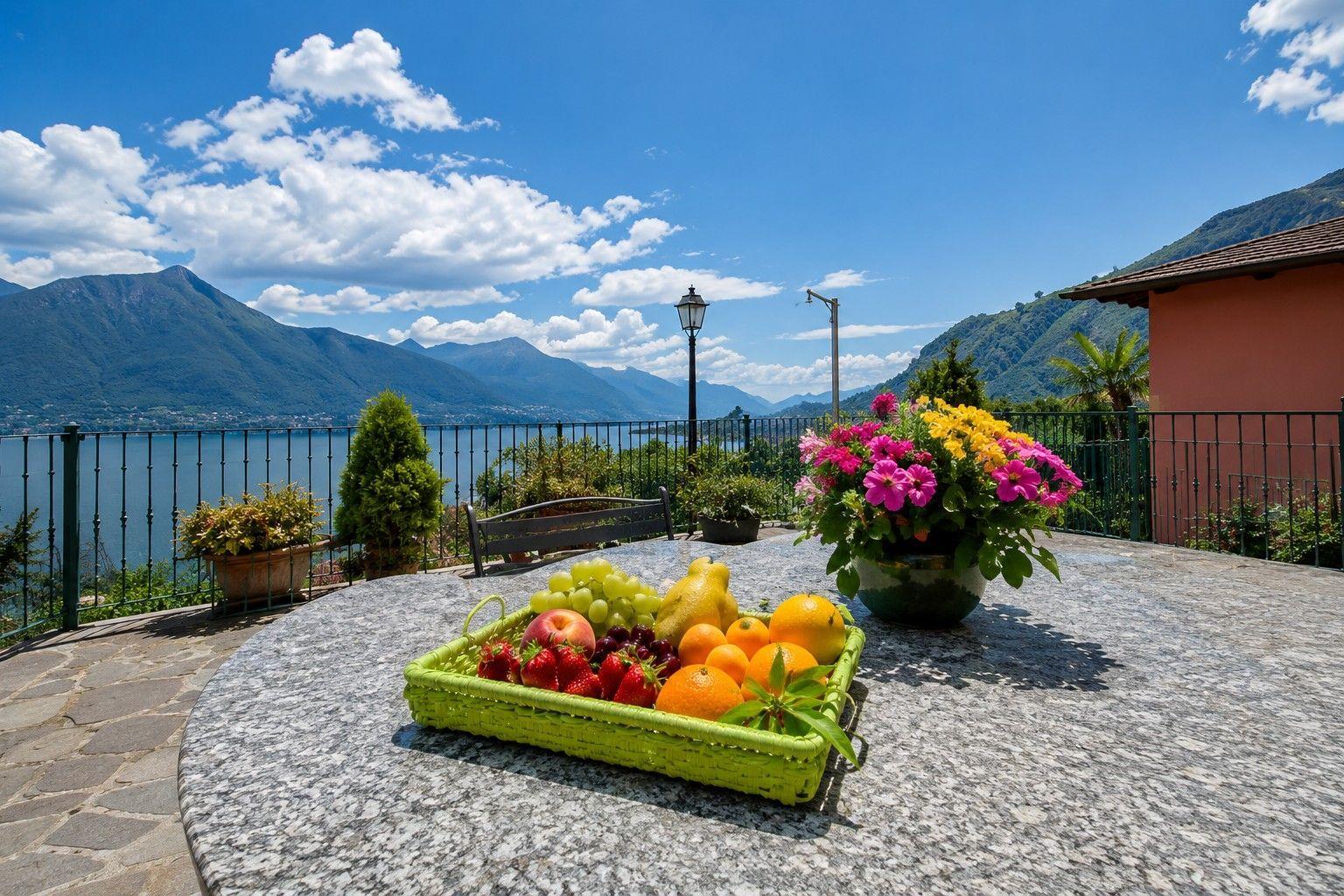 Terrasse mit Obstschale und Blumen, Blick auf See und Berge.