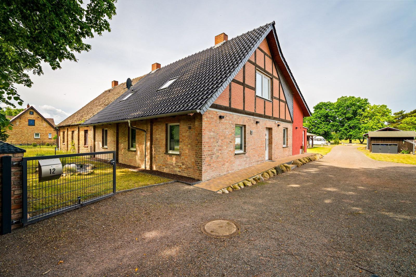 Haus mit rotem Anstrich und Ziegeldach, umgeben von Grünflächen und einem Zaun.