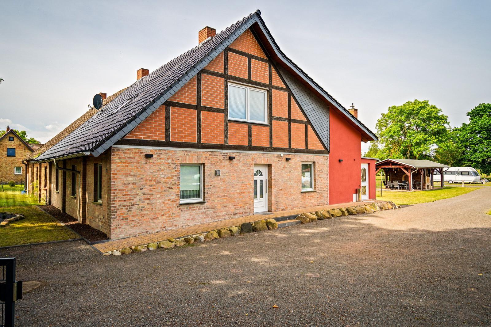 Haus mit Backsteinfassade, rotem Anbau und Schieferdach. Außenbereich mit Grillplatz und Wohnwagen.