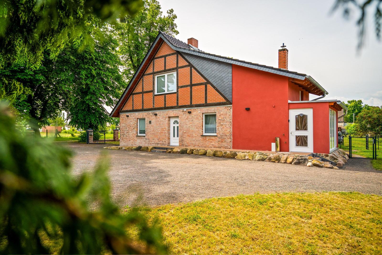 Ein Haus mit roter Wand und Ziegelsteinfassade, umgeben von Grün und einem Kiesplatz.