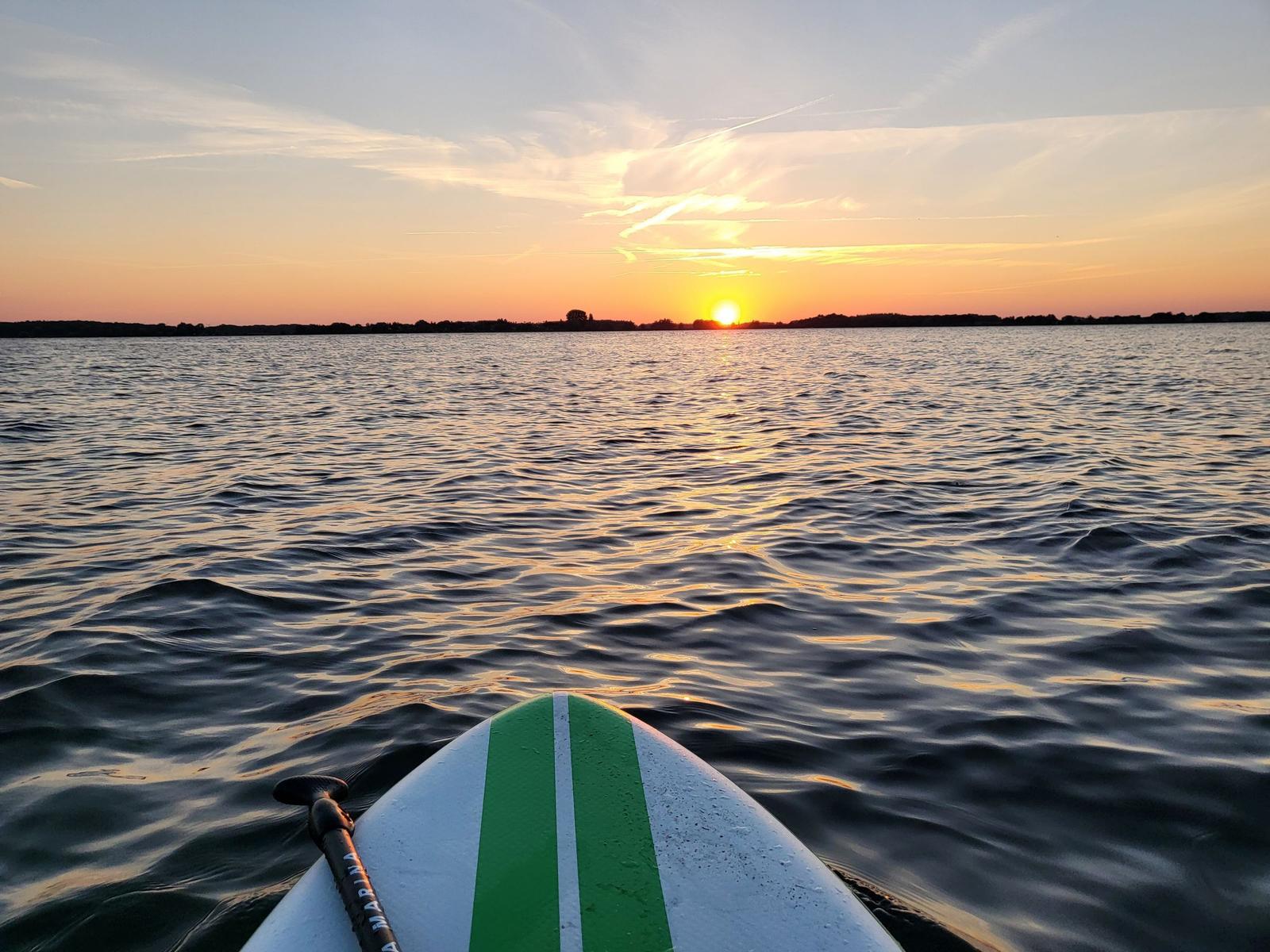 Sonnenuntergang auf dem Wasser mit Stand-Up-Paddleboard im Vordergrund.